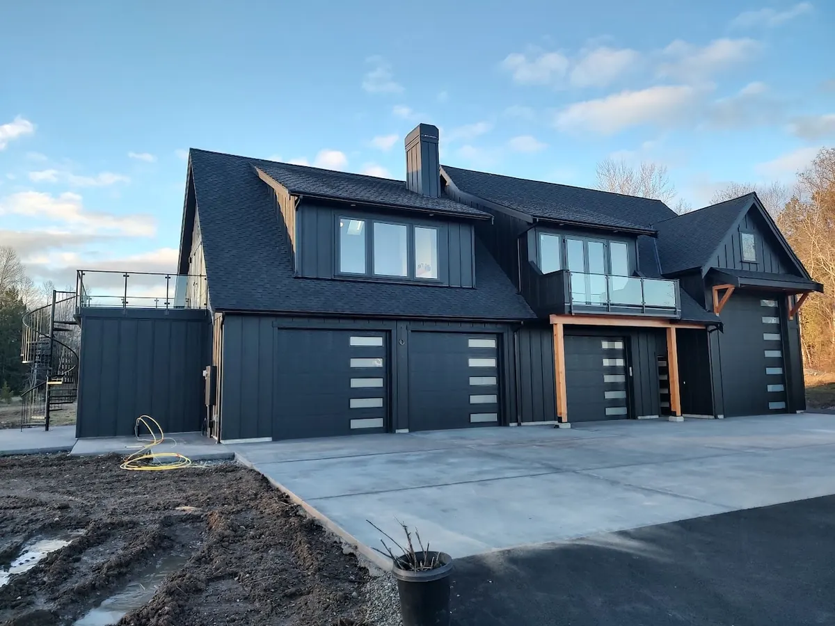 Black board-and-batten home with modern garage doors and a glass-rail deck