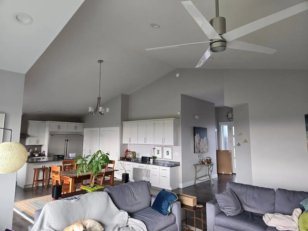 Vaulted great room with soft gray walls, white cabinetry, and a modern ceiling fan