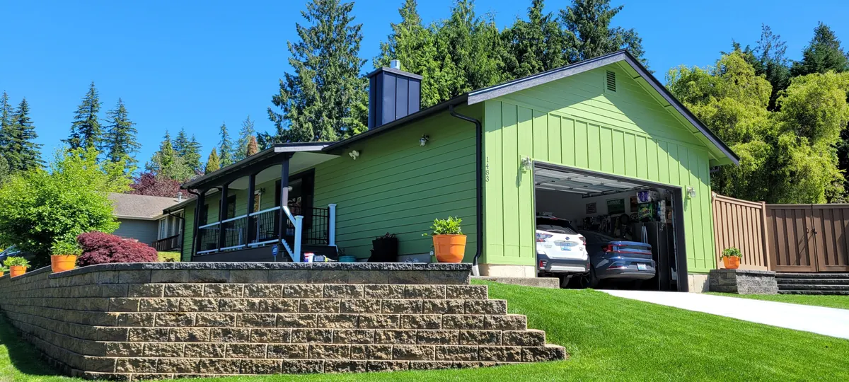 Green rambler with dark trim above a stone retaining wall